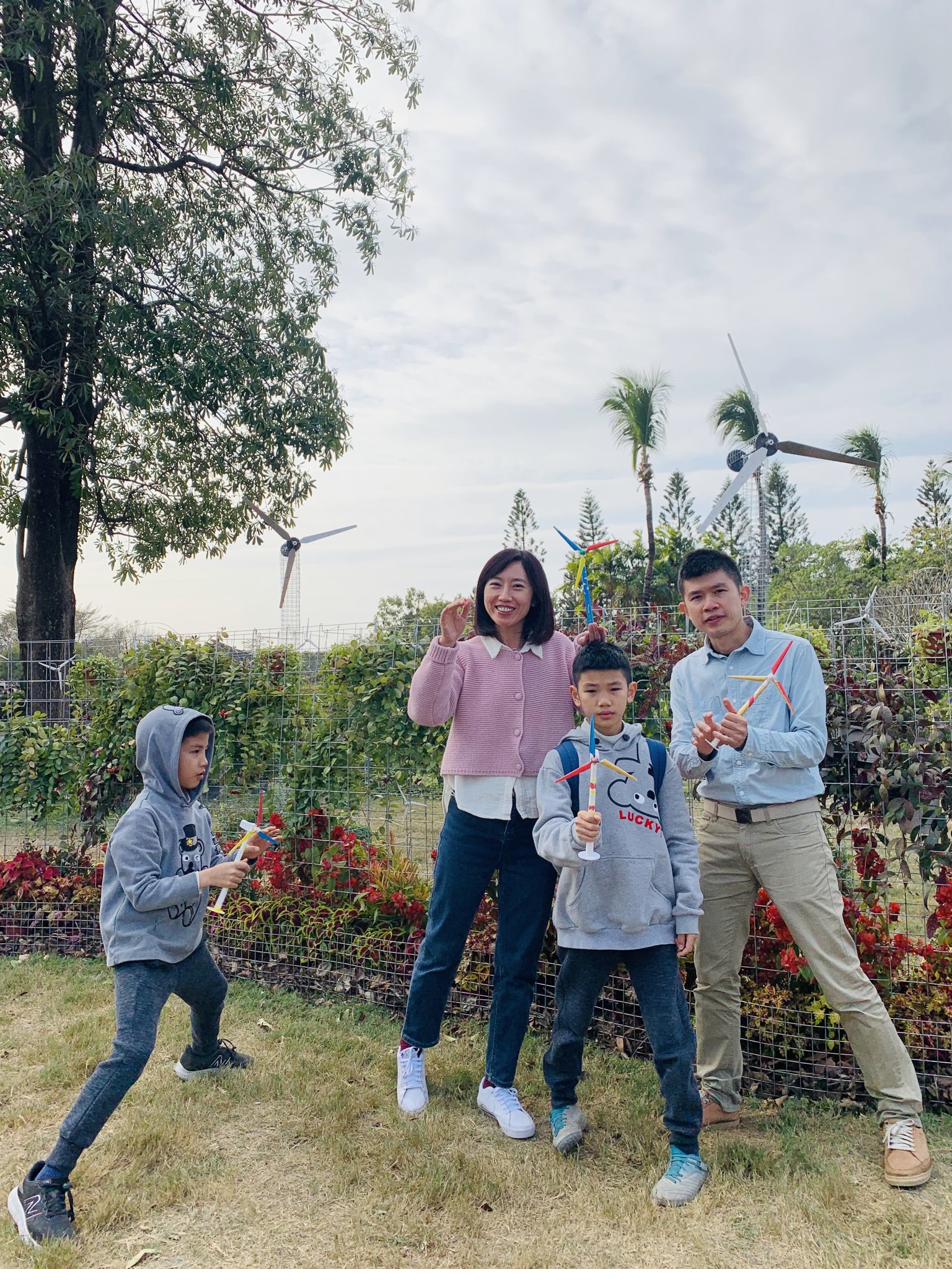 一家四口在彰化公園的鐵件大風機前，每個人手上都拿著一隻親手彩繪的小風機。
