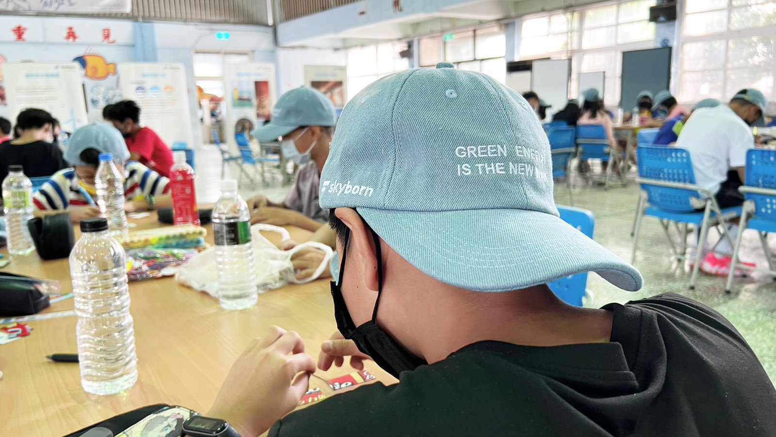 兒童戴著 Skyborn 的湖水綠色棒球帽,帽簷側邊刺繡「GREEN ENERGY IS THE NEW WAY」與 skyborn 字樣。創客營結束後,環保意識化作可日常配戴的物件——成為 take away 的帽子。