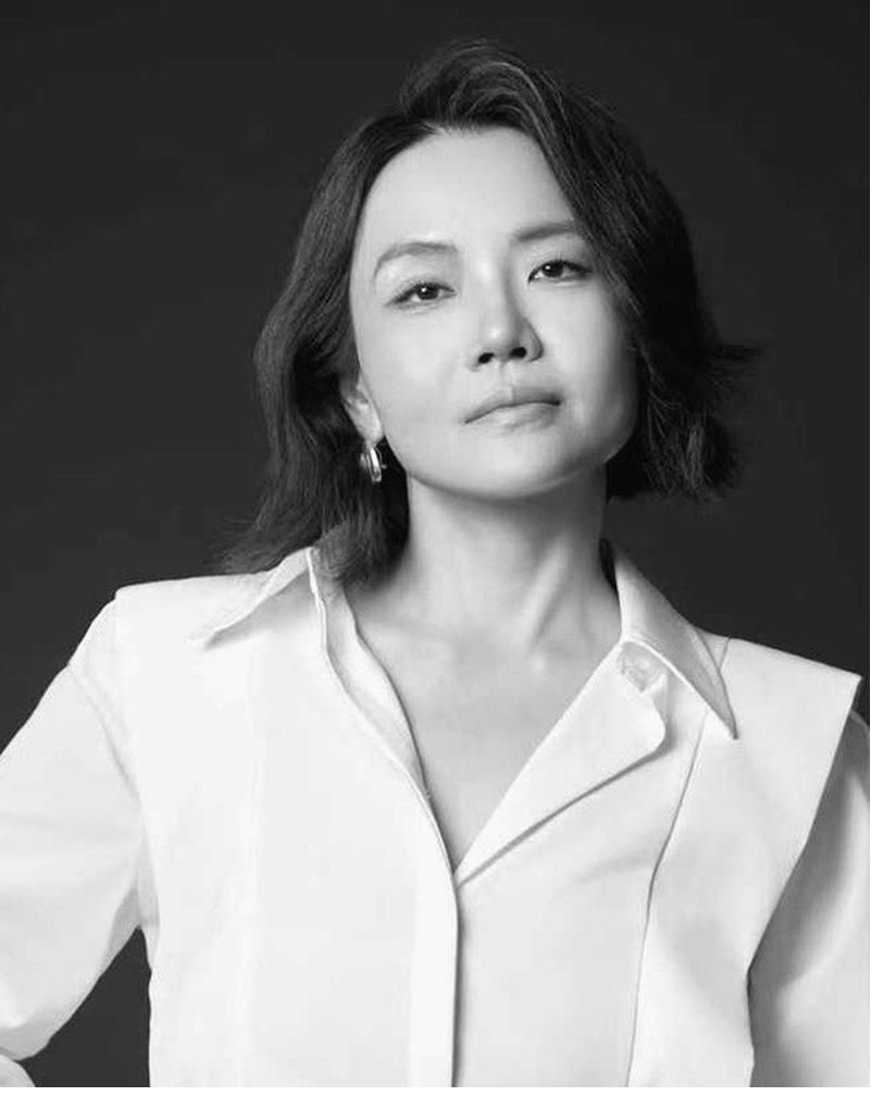 Shanci Hsieh,Acorn 創辦人。穿著白襯衫與黑色皮裙,沉穩站立於深色背景前。
